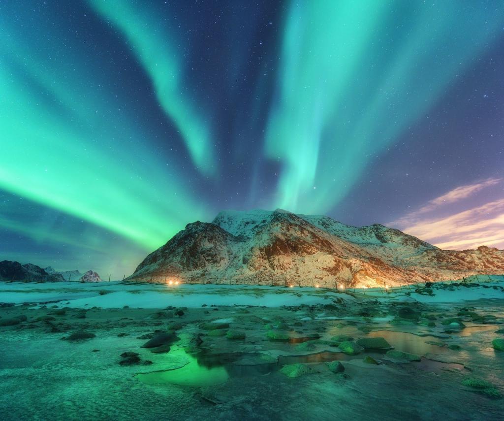 Aurora. Cahaya utara di pulau Lofoten, Norway. Langit berbintang dengan lampu kutub. Landskap musim sejuk malam dengan aurora, laut dengan pantulan langit, batu, pantai berpasir dan gunung. Aurora borealis hijau