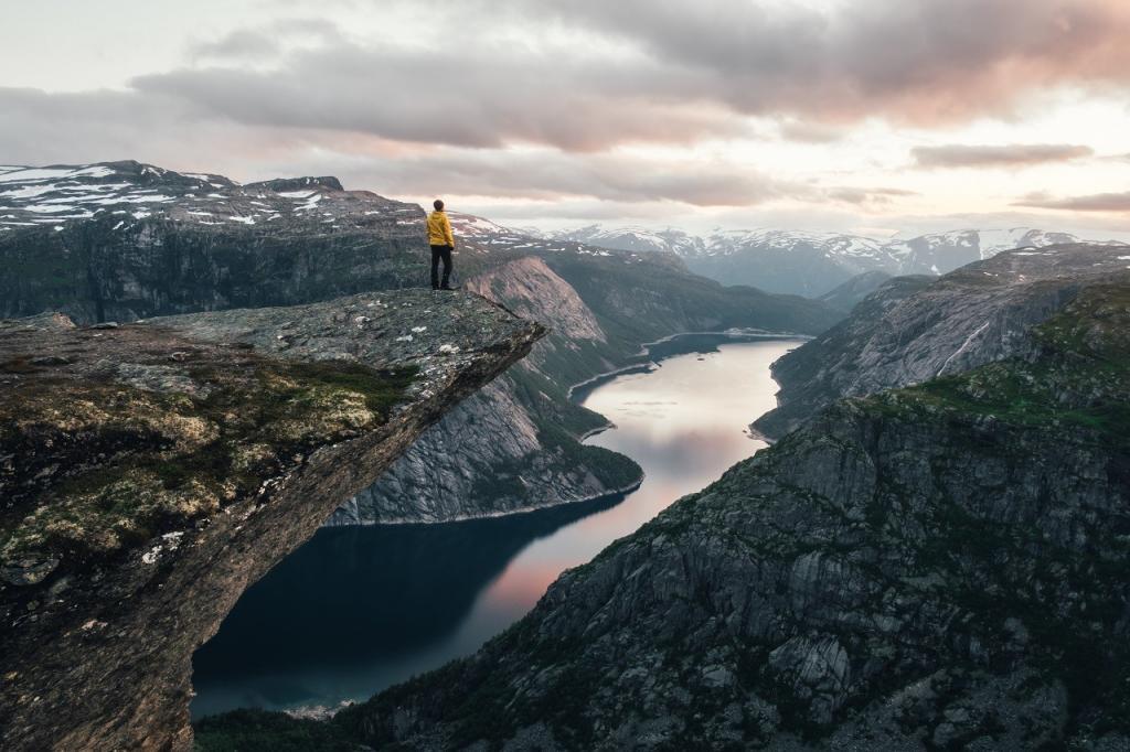 Breathtaking view of Trolltunga rock - most spectacular and famous scenic cliff in Norway. Picturesque landscape with sunset sky and clear lake