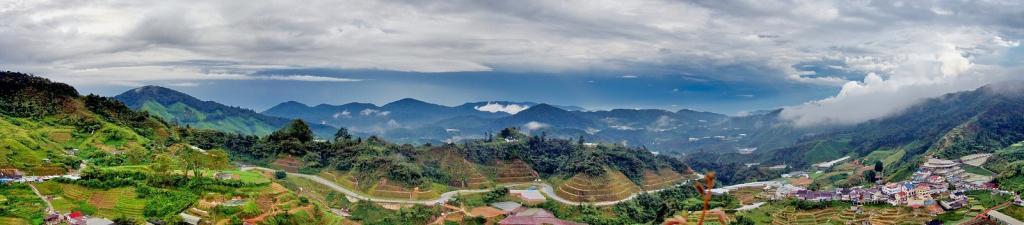 Panorama of Cameron Highlands with visible tea plantations and human settlements under blue sky with white clouds