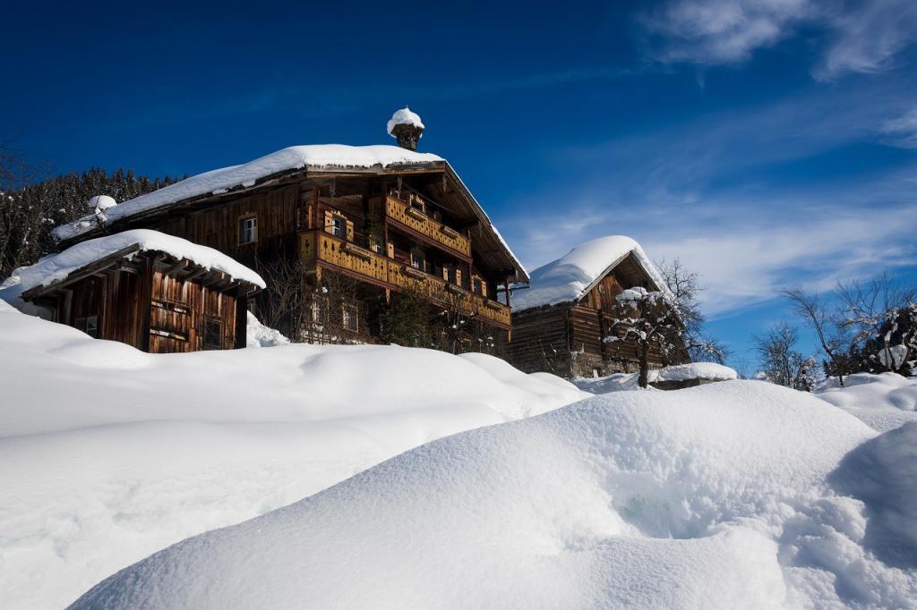 Two wooden ski chalets and a small barn surrounded by and covered with snow under a blue sky in winter in a ski resort in Tyrol, Austria.