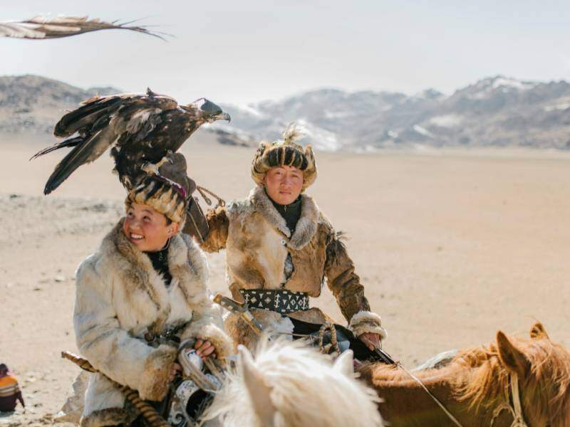 Mongolian eagle hunters riding horses on mountainous terrain